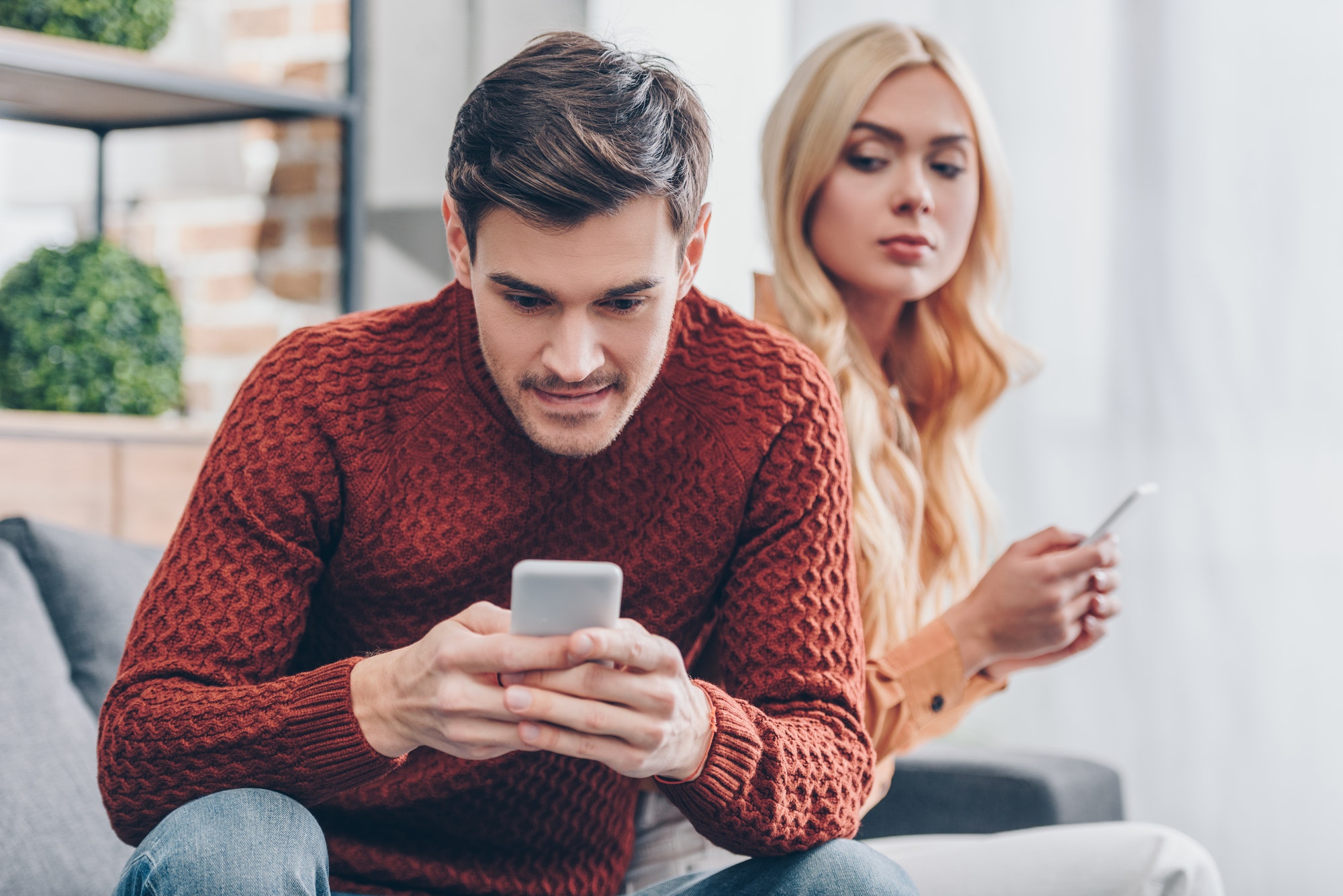 woman peaking on her husbands phone out of jealousy 
