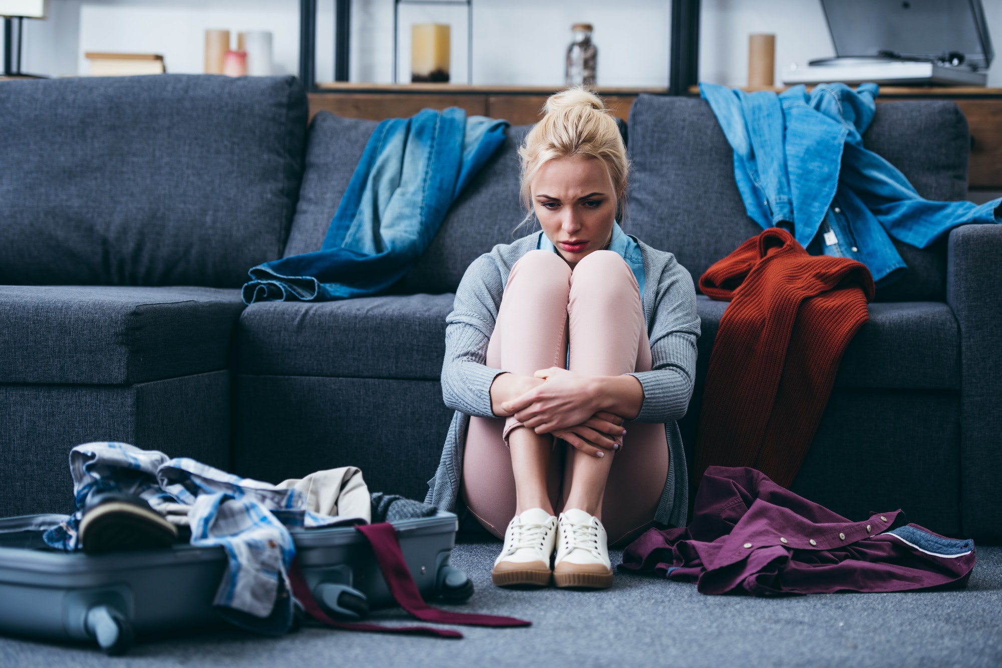 sad woman sitting with scattered clothes and suitcase after breaking up with boyfriend