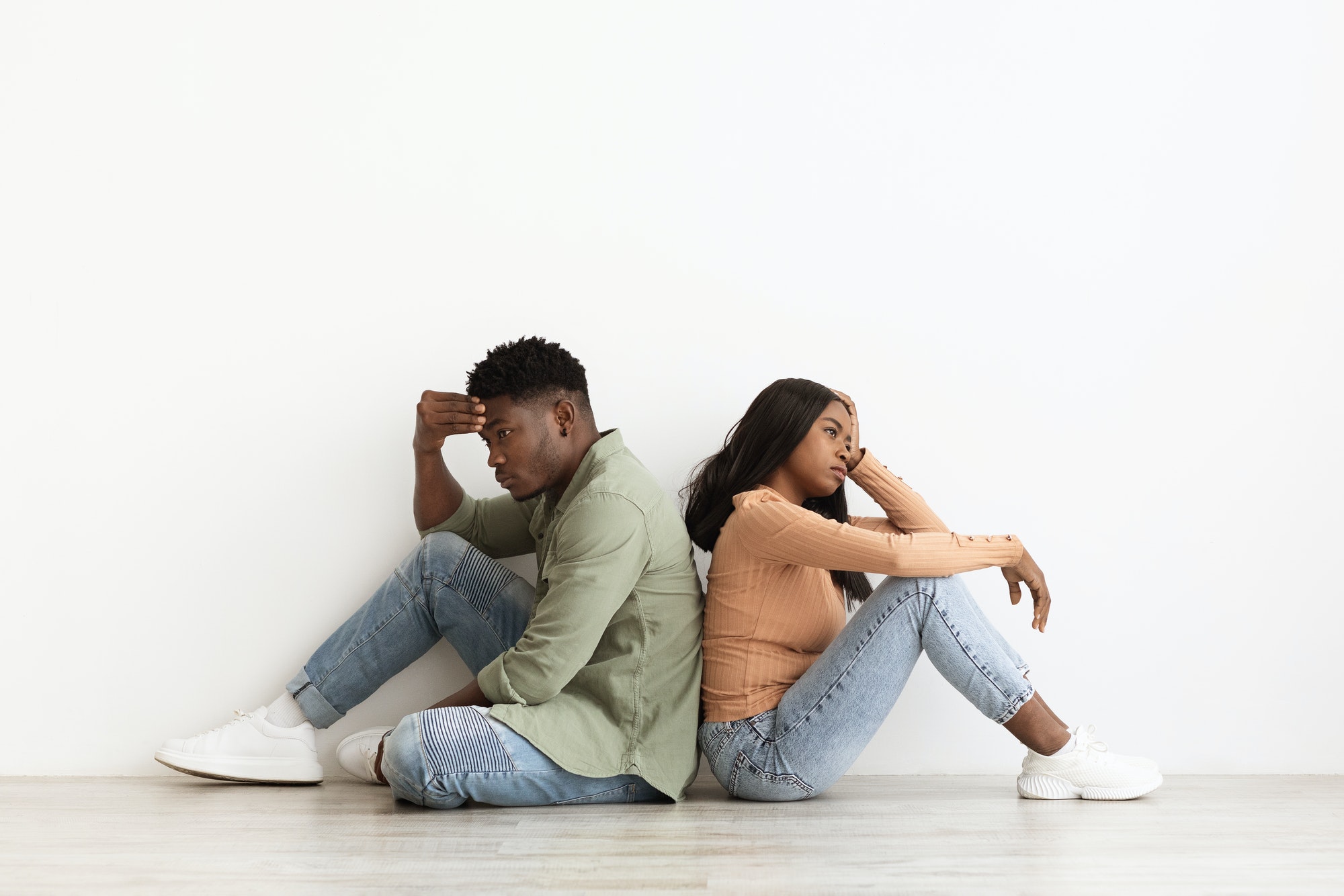 Upset african american couple sitting back to back on floor